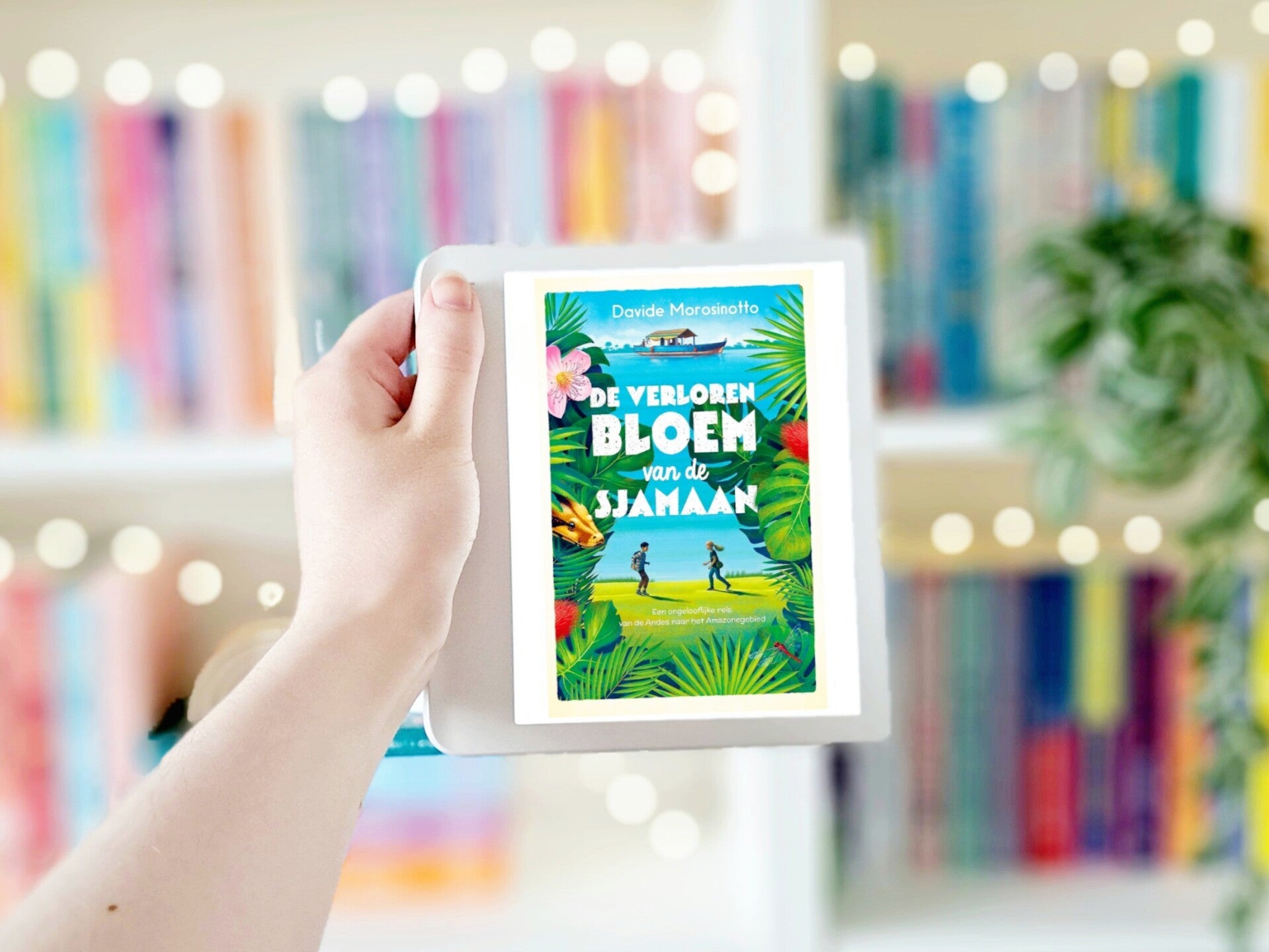 Een witte hand houdt 'de verloren bloem van de sjamaan' door Davide Morosinotto omhoog tegen een witte muur. Foto bij recensie door turnthepages.nl