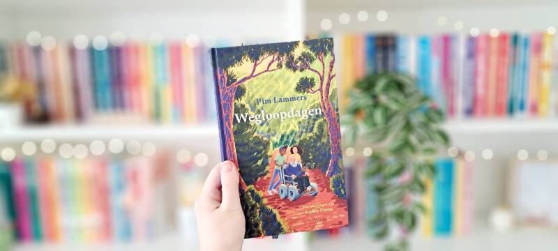 Een witte hand houdt 'wegloopdagen' van Pi Lammers omhoog voor een wazige kleurrijke boekenkast met lichtjes. | Recensie door turnthepages.nl | Rolstoelgebruiker, chronisch ziek en disabled bookstagrammer, neurodivergente boekblogger met ADHD.