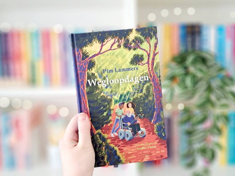 Een witte hand houdt 'Struikmeisje' van Tineke Honingh omhoog voor een kleurrijke wazige boekenkast met lichtjes. Foto bij own-voices recensie door turnthepages.nl Rolstoelgebruiker en disabled bookstagrammer en blogger.