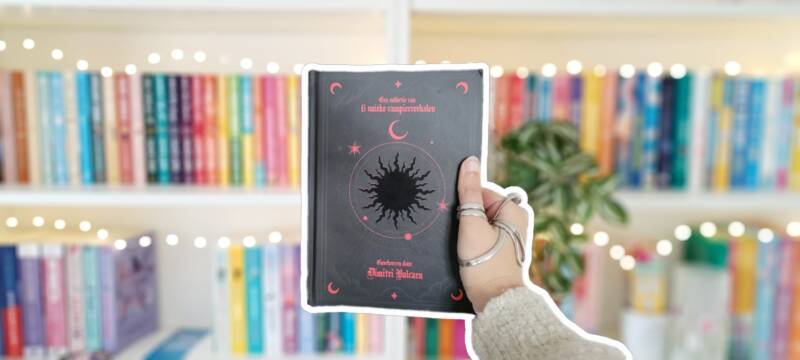 Quinty's witte hand omhuld met zilveren ortheses houdt de zwarte hardcover van 'Era van Bloed' van Dimitri Balcaen omhoog voor een kleurrijke wazige boekenkast met lichtjes. 