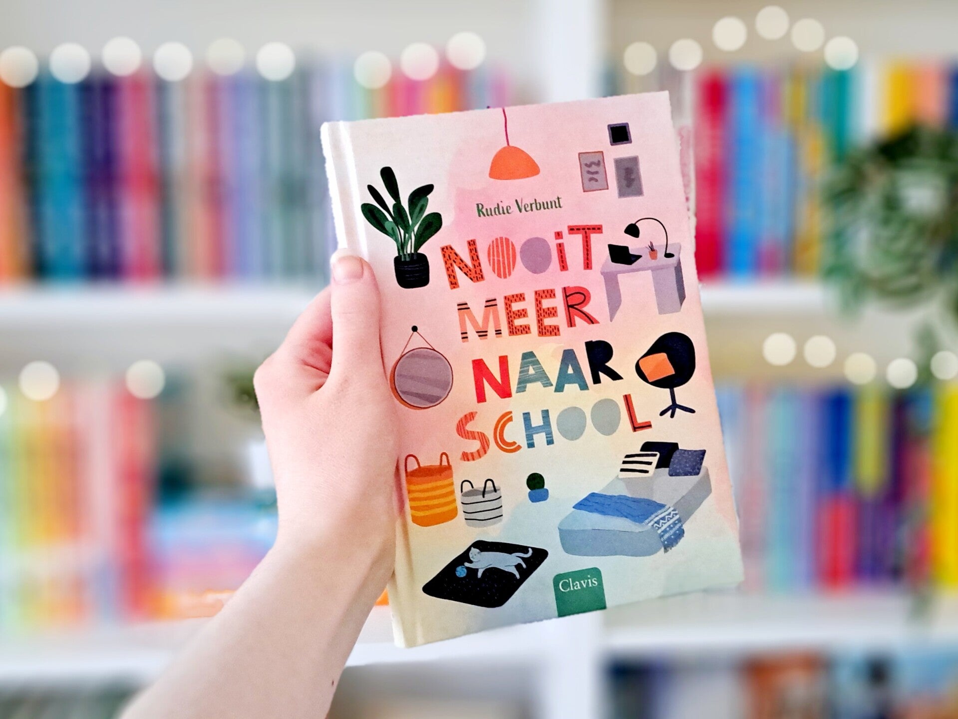 Een witte hand houdt 'Nooit meer naar schol' van Rudie Verbunt omhoog voor een kleurrijke wazige boekenkast met lichtjes. Foto bij recensie door turnthepages.nl