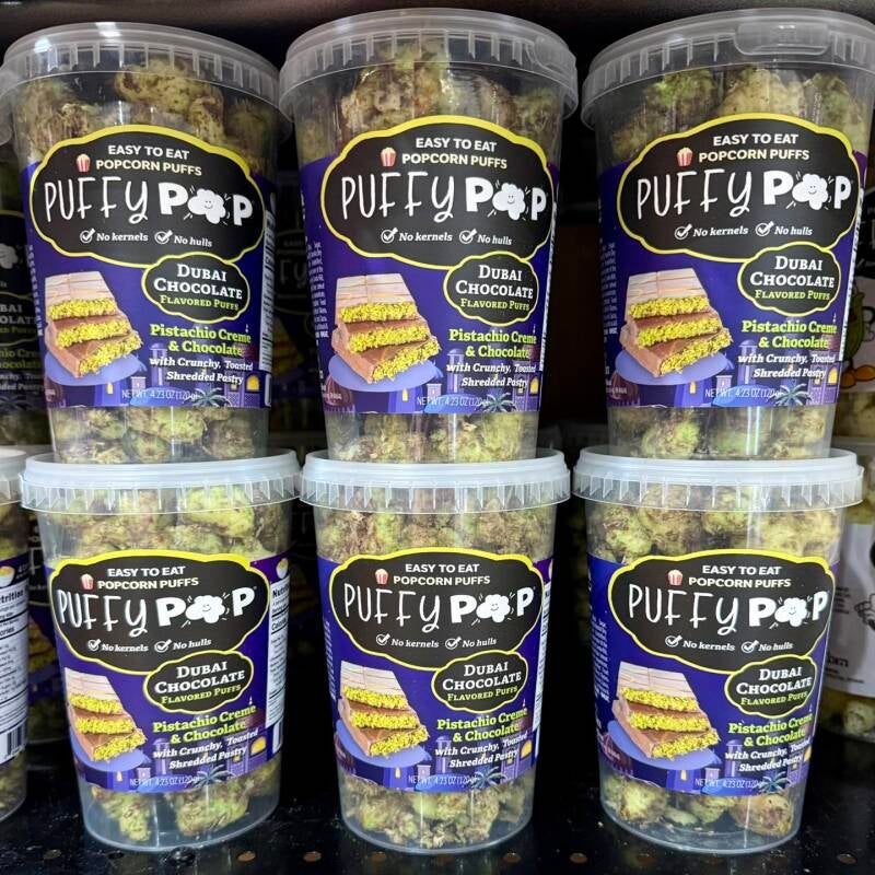 Six tubs of Tethan’s Dubai Chocolate Crac Corn stacked 3x3, labels facing out like a store shelf display.