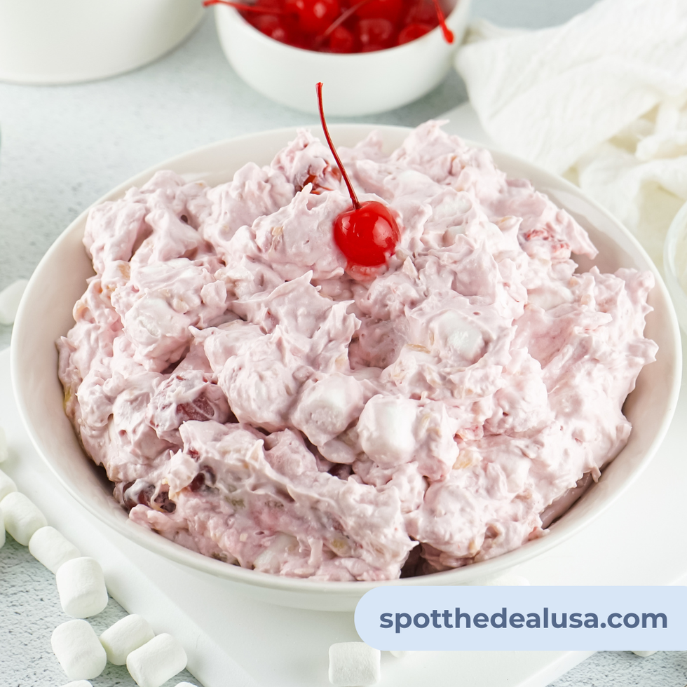 Bowl of traditional cherry fluff dessert topped with cherries and mini marshmallows, served chilled with a spoon on tablecloth.