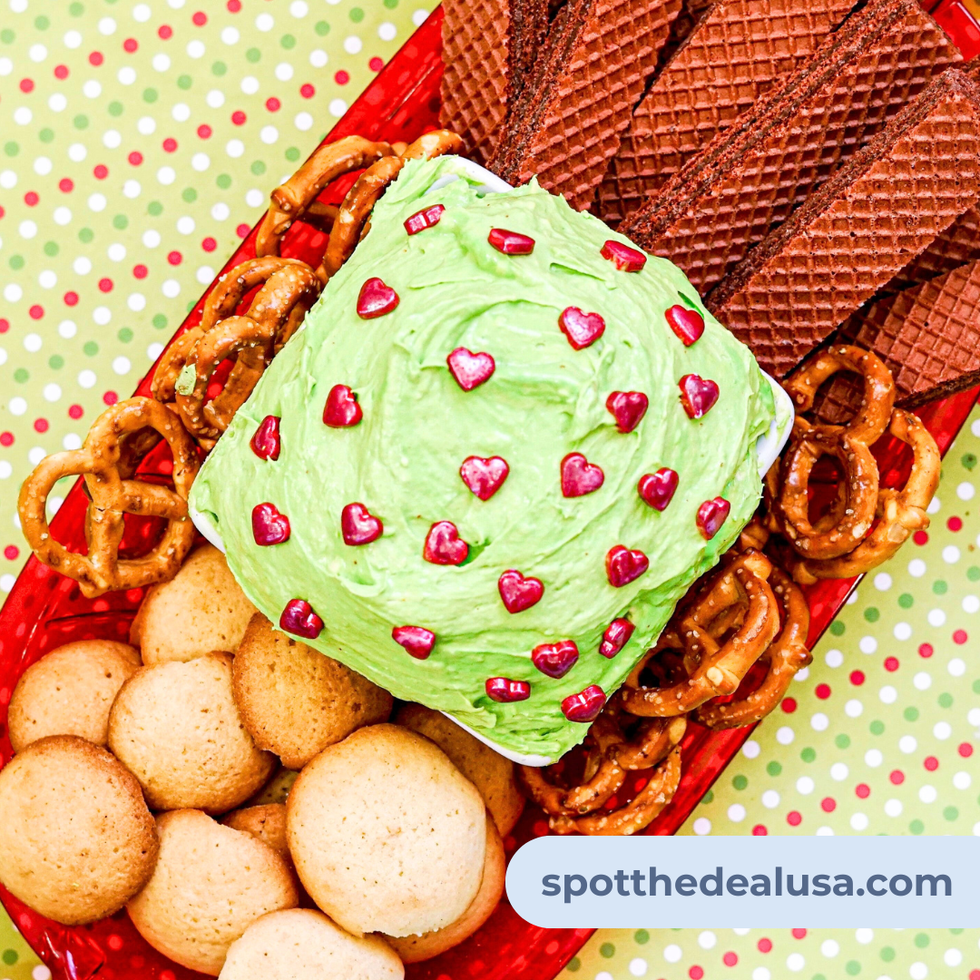 A bowl of bright green Christmas Dunkaroo Dip topped with red heart sprinkles, surrounded by vanilla wafer cookies on a festive holiday tray.
