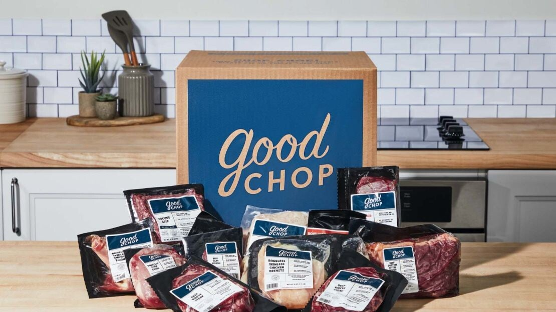 A Good Chop cardboard delivery box with a variety of fresh meats arranged in front, including steak, chicken, and pork cuts.