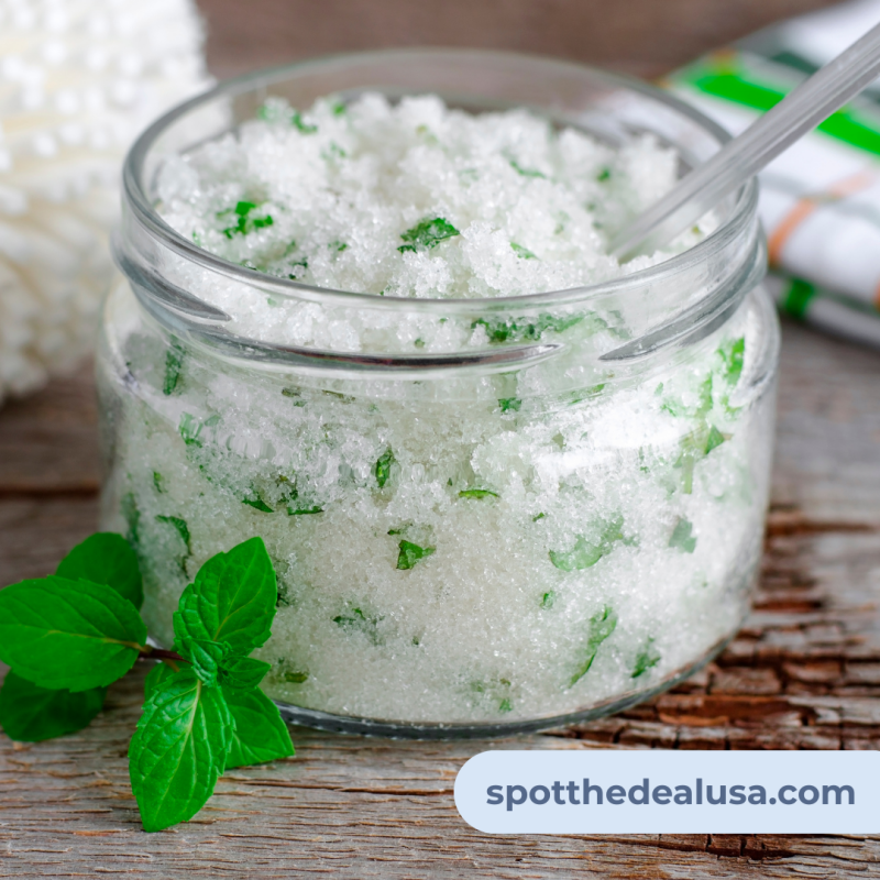 Glass jar filled with homemade mint sugar scrub, surrounded by fresh mint leaves on a white background — perfect for skincare or gifting.