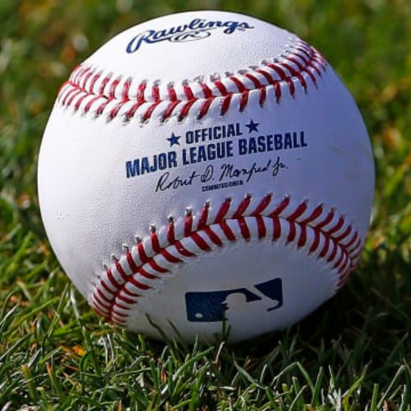 Official MLB baseball resting on the grass in a baseball field, centered and close-up.