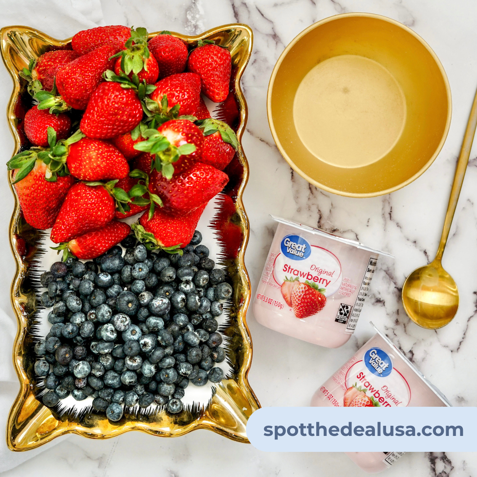 Platted Strawberries and blueberries next to a bowl, spoon and two ups of Great Value Original Strawberry Yogurt.