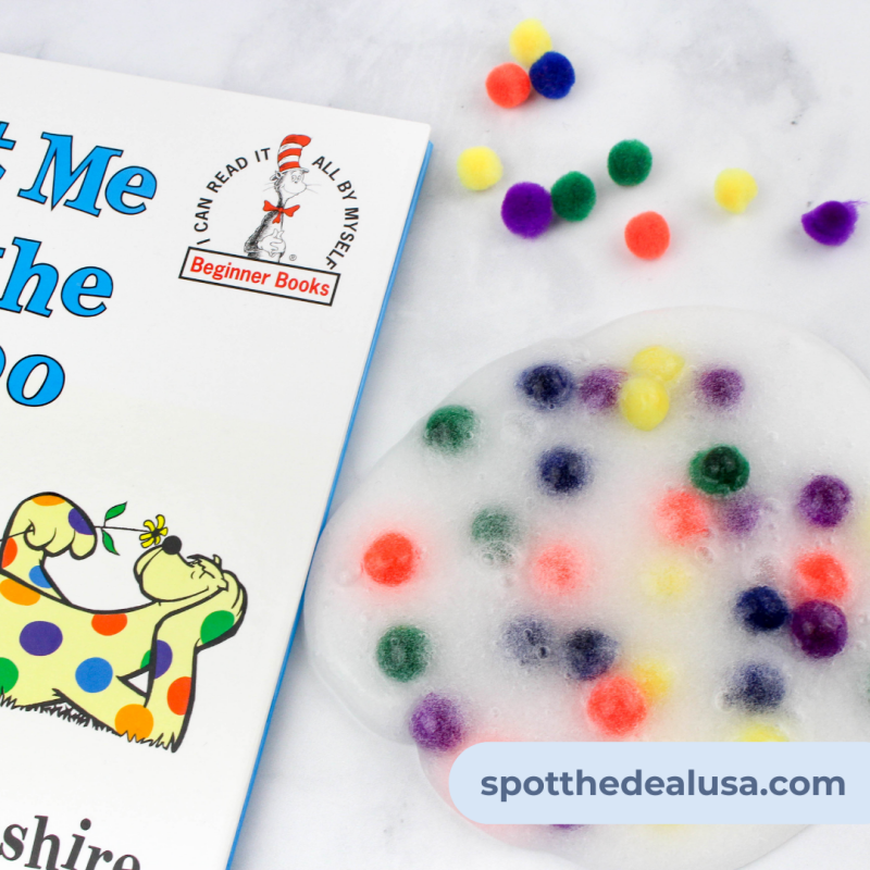 Clear DIY slime with colorful pom poms spread out on a table next to a copy of Put Me in the Zoo by Dr. Seuss.