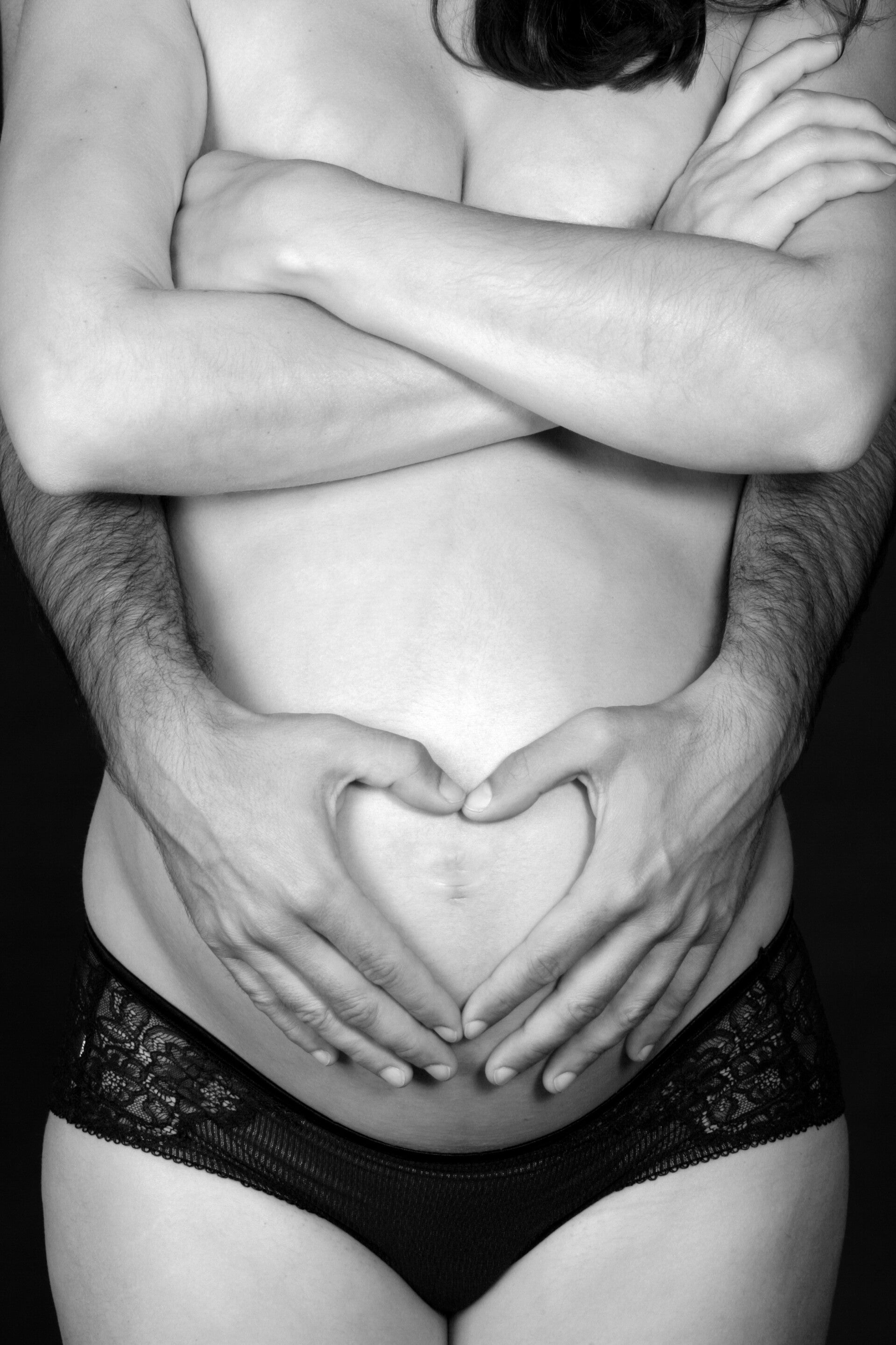 Hände eines Paares formen ein Herz auf dem nackten Babybauch.