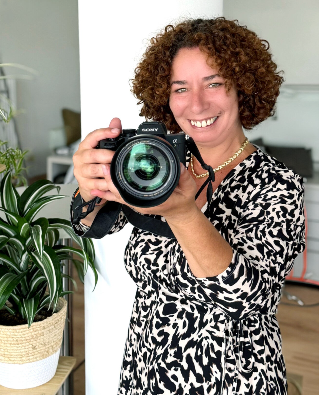 Fotografin Patricia Villafana Moya, Inhaberin von FOTO Villa in Germering, hat eine Kamera in der Hand und blickt glücklich in eine andere Kamera.
