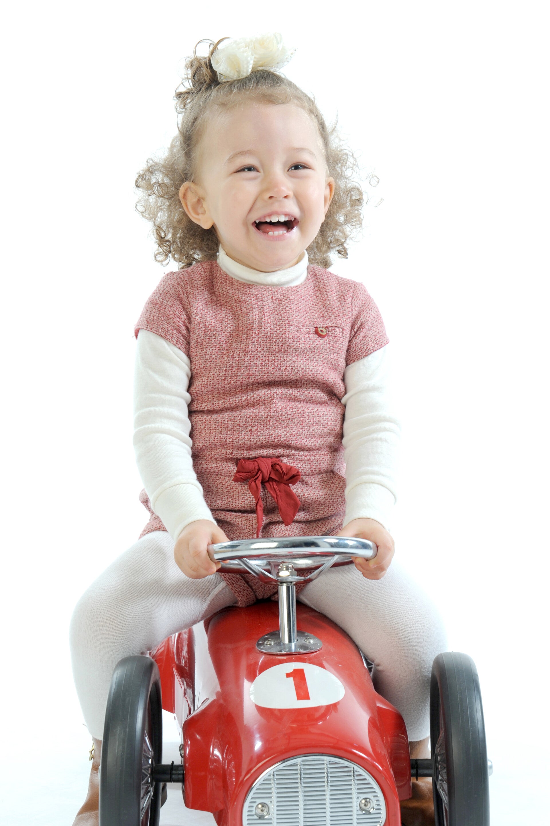 Kleines Mädchen lacht fröhlich auf einem roten Spielzeugauto im Fotostudio.