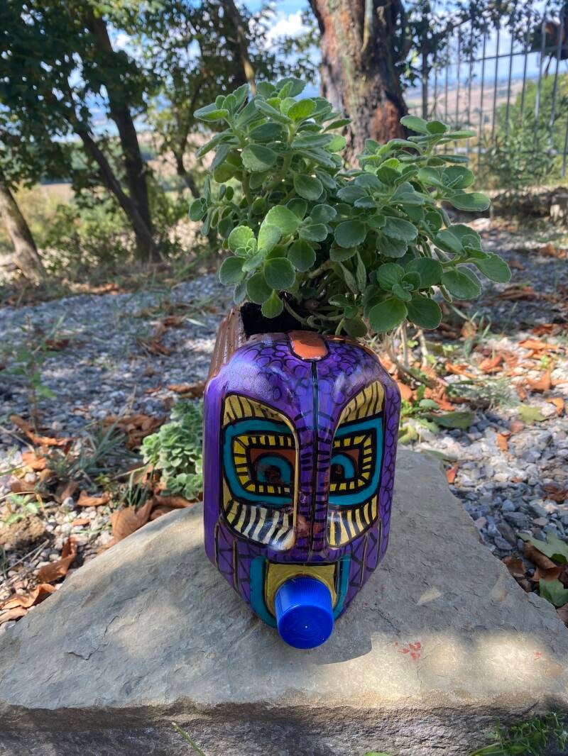 A fun planter for the garden. It is made from a large plastic water container sprayed with paint then details are added using acrylic markers. Featuring a face.  A hole is cut in the top. This is filled with soil and then herbs are planted. 