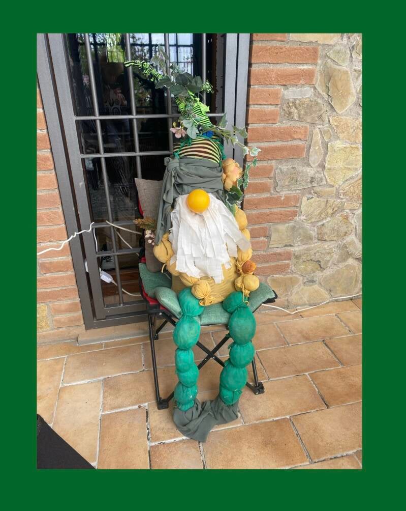 A large homemade gnome sat on a chair on the patio.  Crafted from upcycled materials.  