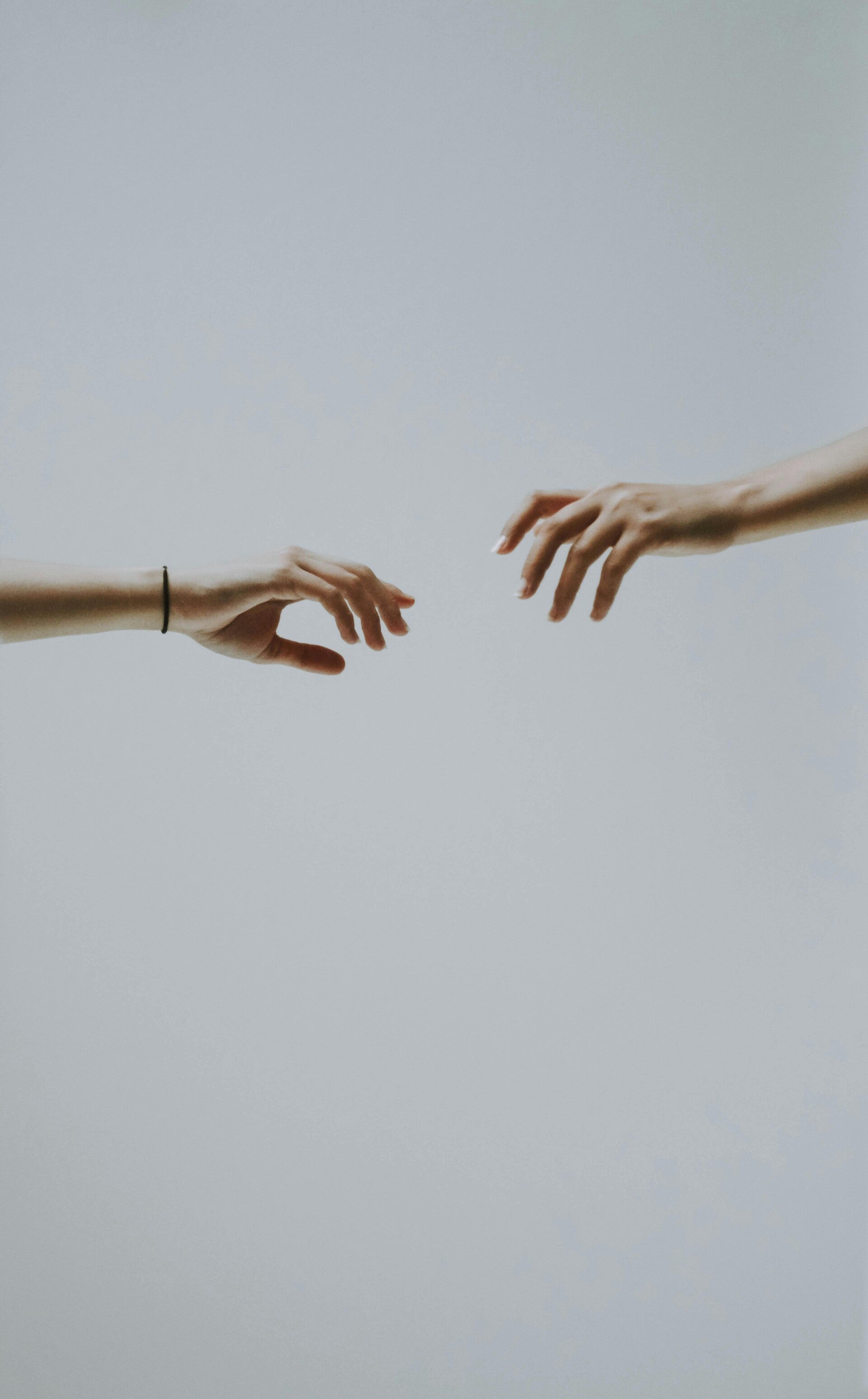 Image of two hands reaching for each other against  a plain grey background.
