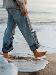 A person in jeans walking barefoot at the sea edge through