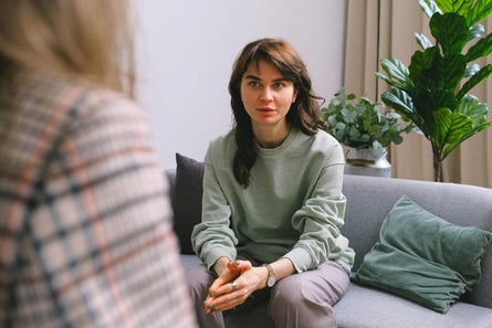Woman in conversation on a gray couch in a calm, indoor setting.