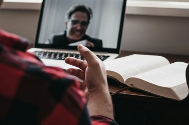 Counsellor conducting an online counselling session, viewing and interacting with a client on a video call, with an open book on the desk.