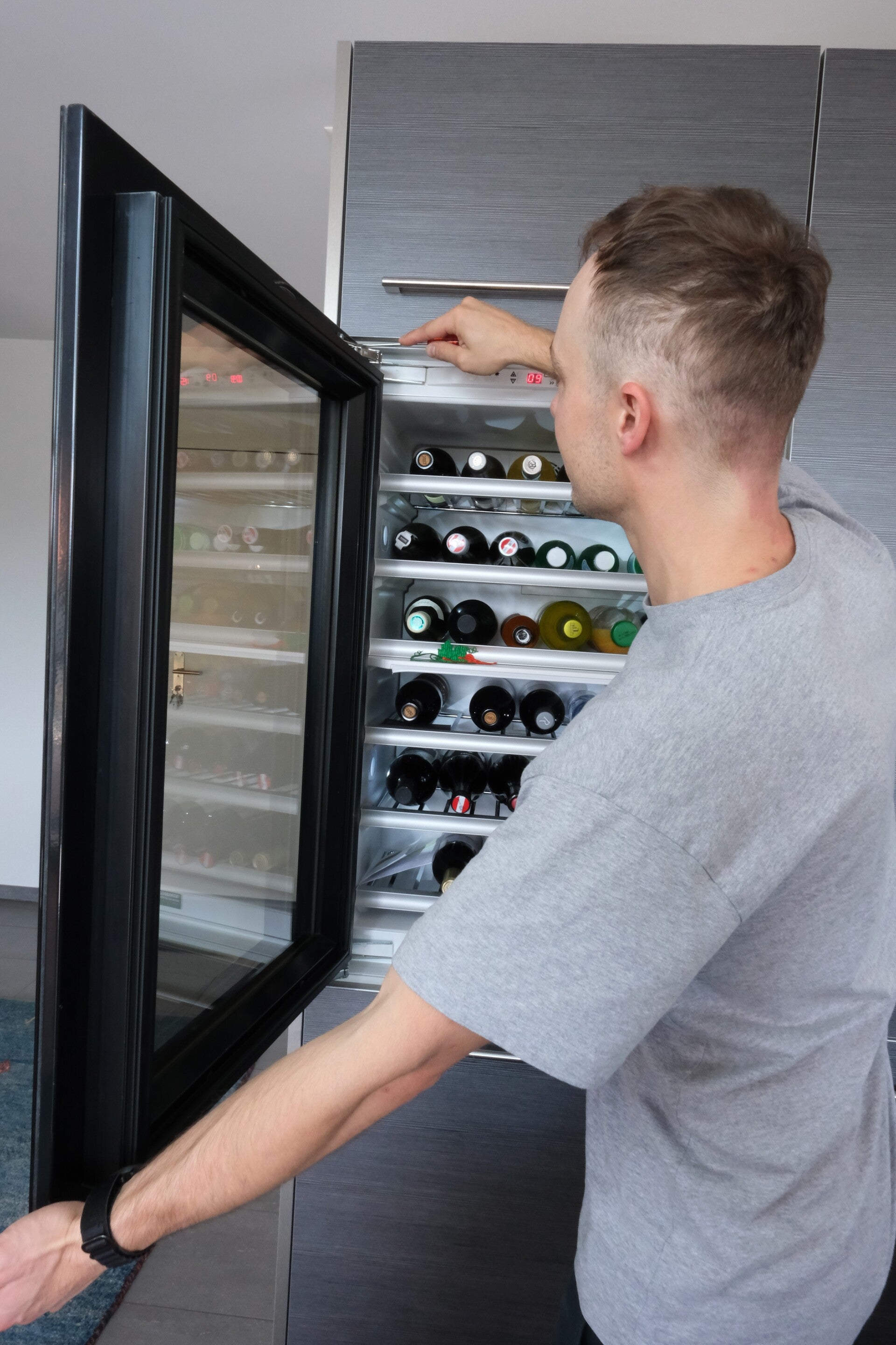 Techniker ustalliert oder repariert die Türscharniere eines gefüllten Weinkühlschranks.