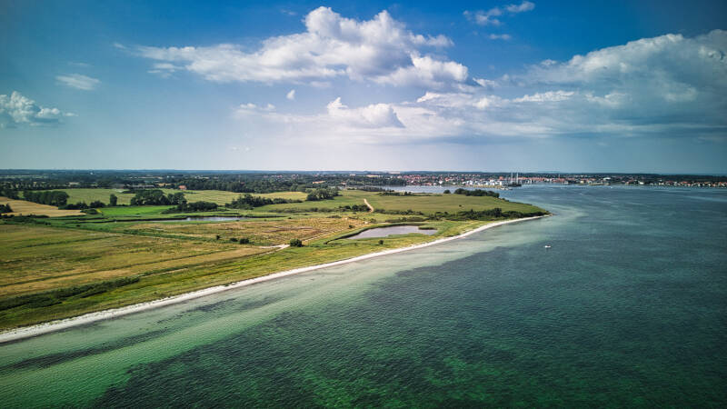 Dronefoto af kystlinje med grønne marker og blå himmel, tagget af Scenes From Above