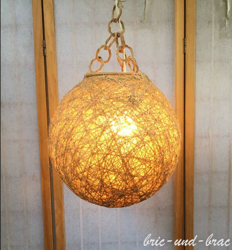 Runder Lampenschirm aus feinem Rattan-Geflecht und hat eine Kugelform mit einem Durchmesser von 35 cm. Die Aufhängung erfolgt an drei „Ketten“ mit ineinander geflochtenen Gliedern aus dem gleichen Material