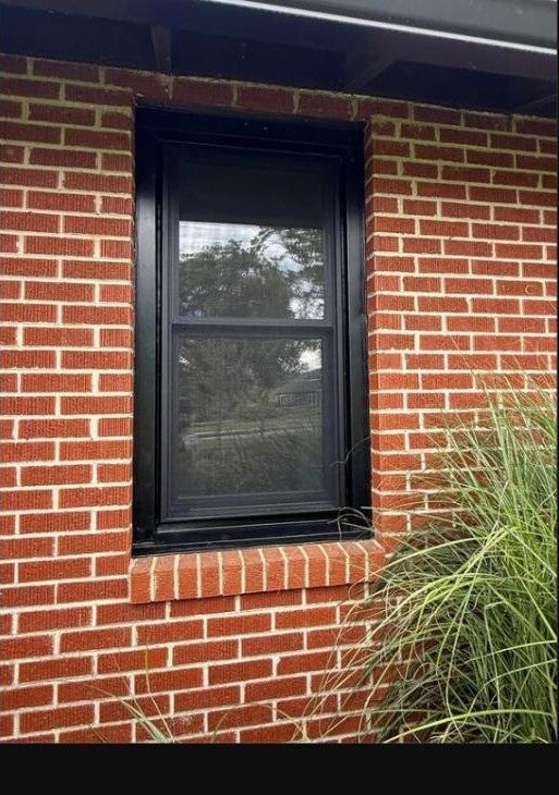 Black-framed replacement window installed on a brick home exterior