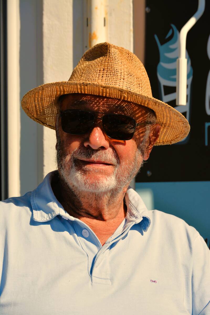 c'est le portrait d'un homme assis au nomad café à noirmoutier  avec un joli chapeau en paille