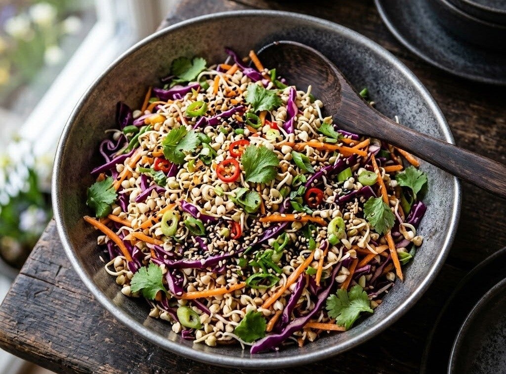 En skål fylld med en asiatisk sallad med rödkål, morötter, chili och bovetegroddar odlade från egna bovetefrön, stående på ett mörkt träbord med en träsked.