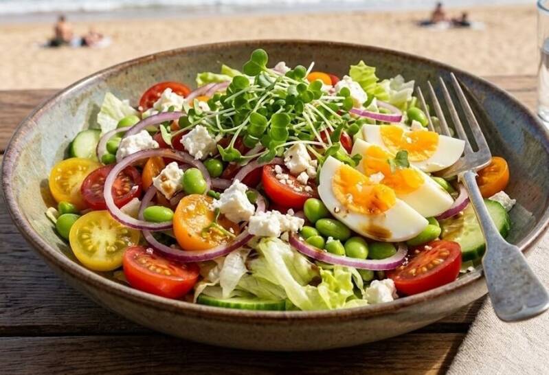 En skål med en färgglad sallad med ägg, tomater, fetaost och kålskott odlade från egna fröer till kinesisk kålfrö, stående på ett bord med en gaffel.