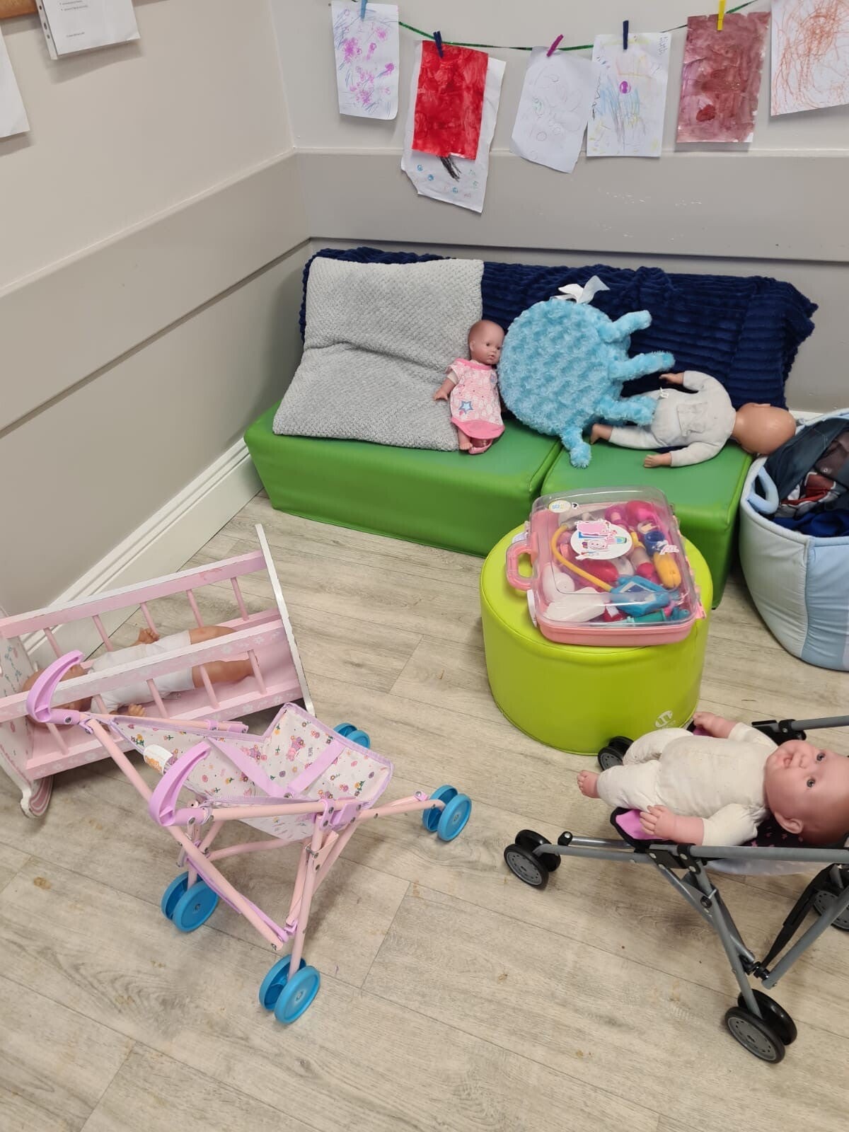 An area of Room 2 with a sofa and dolls cot and 2 pushchairs and lots of dolls.