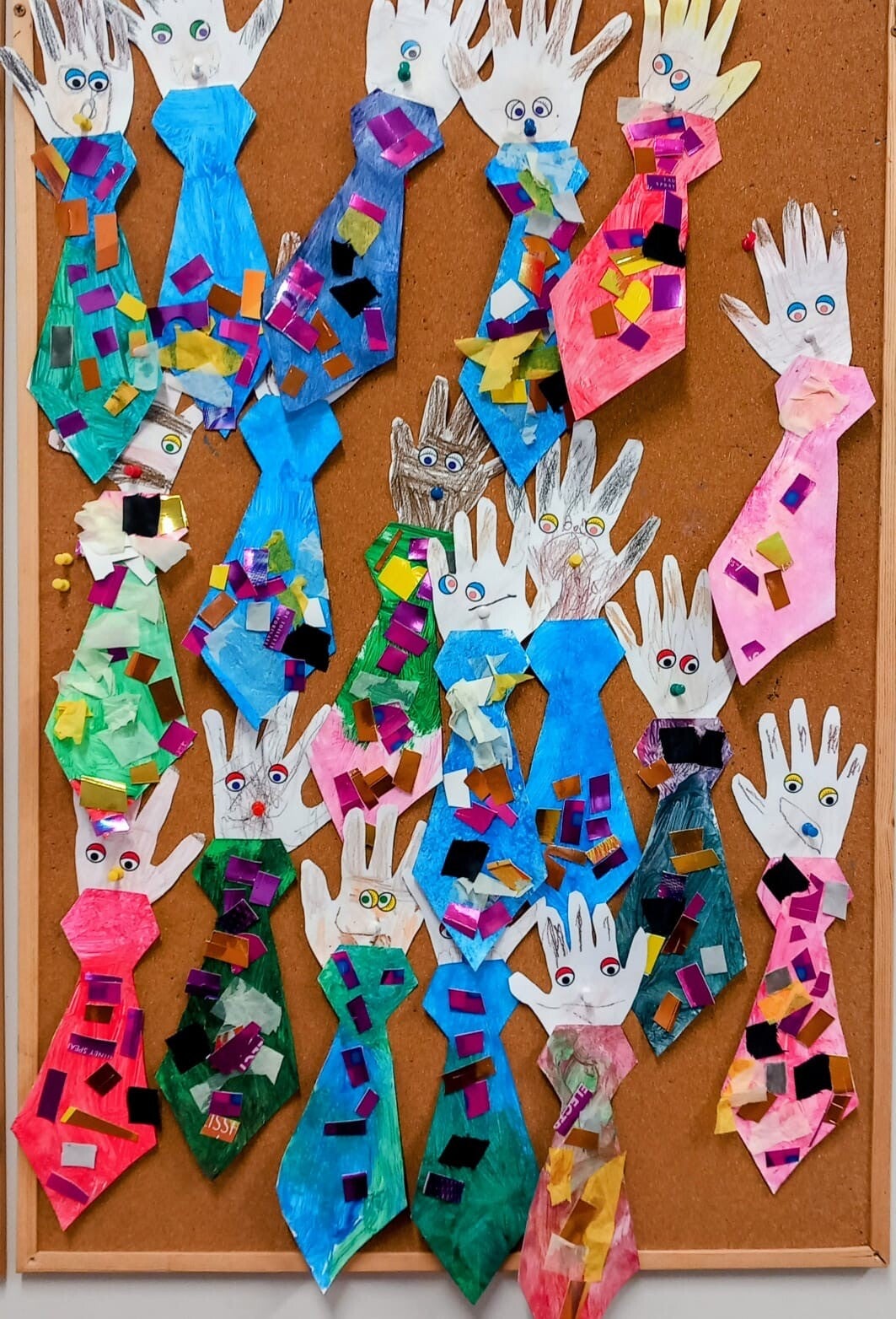 Childrens artwork for fathers days shows paper hands with faces on them attached to coloured and decorated paper suit ties.
