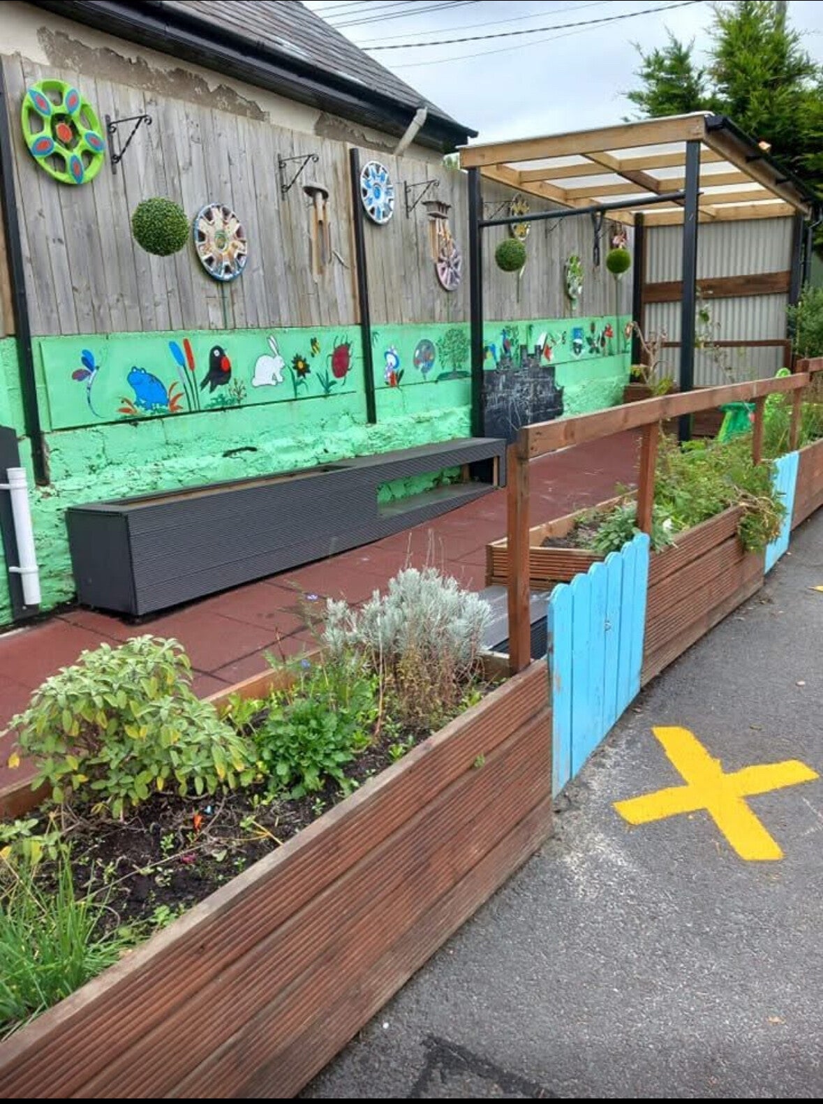 Outdoor area of Rathduff Community Playschool with colurful wooden wall, boxed flowers and little wooden blue gate.
