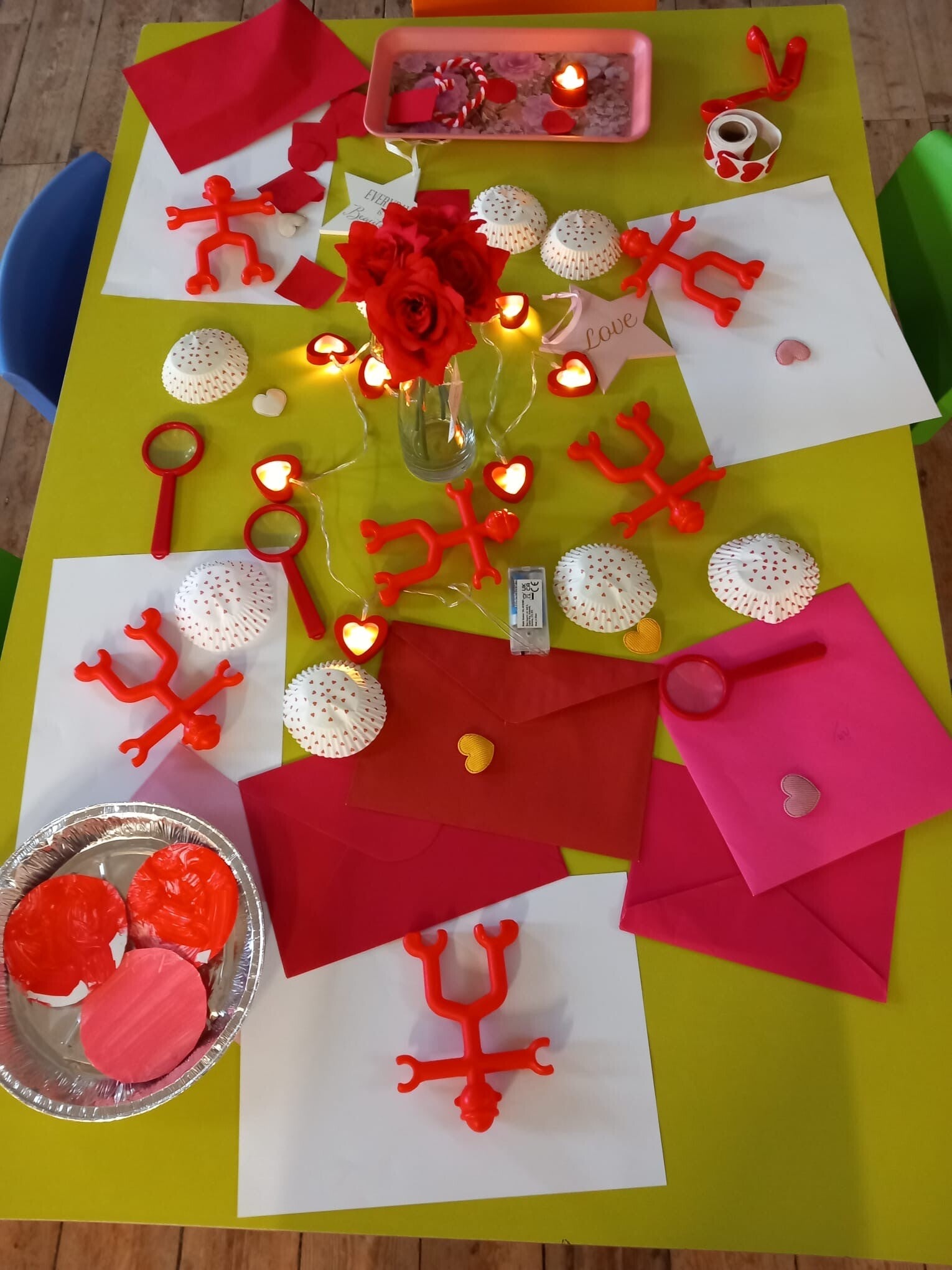Valentines week at Playschool . The table shows lots of red and pink items on a green table with lots of fairly lights and hearts.