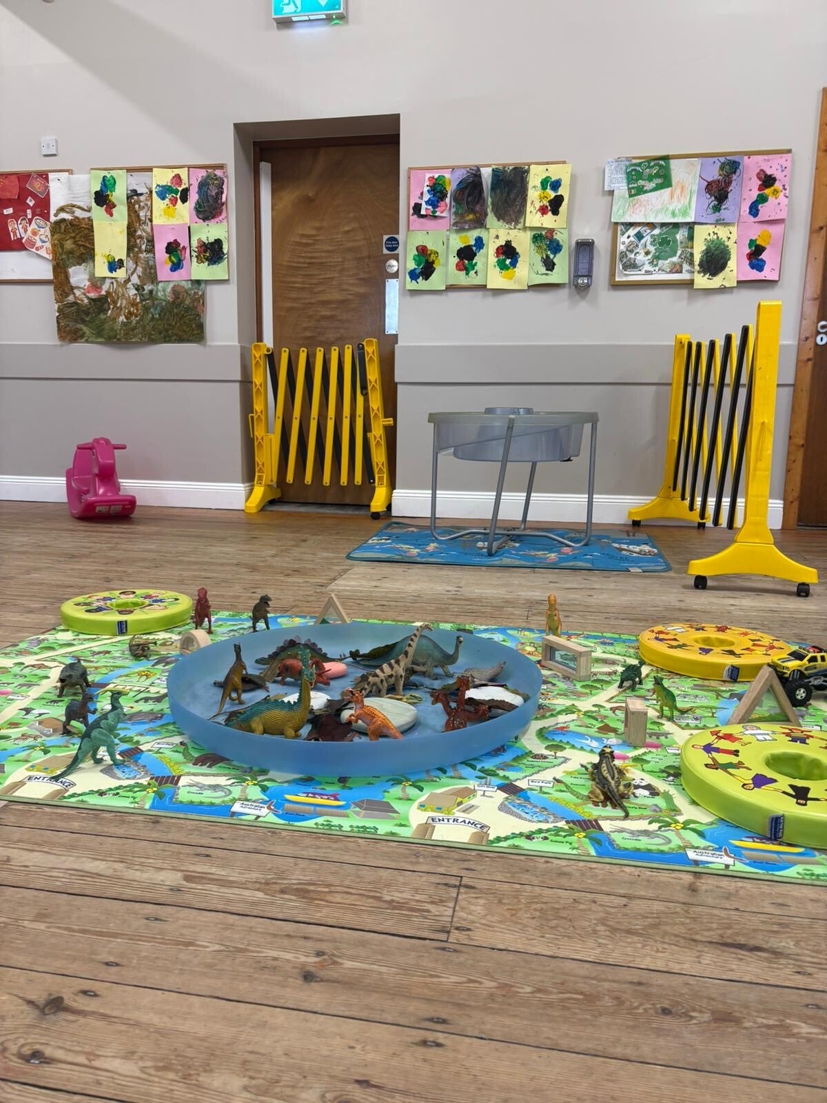 a play area with a colourful playmat on floor and lots of toy dinasaurs on the mat.