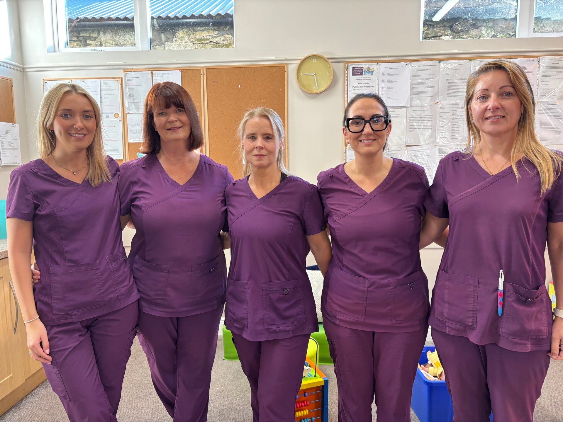 5 members of staff wearing purple uniform smiling and linked arms