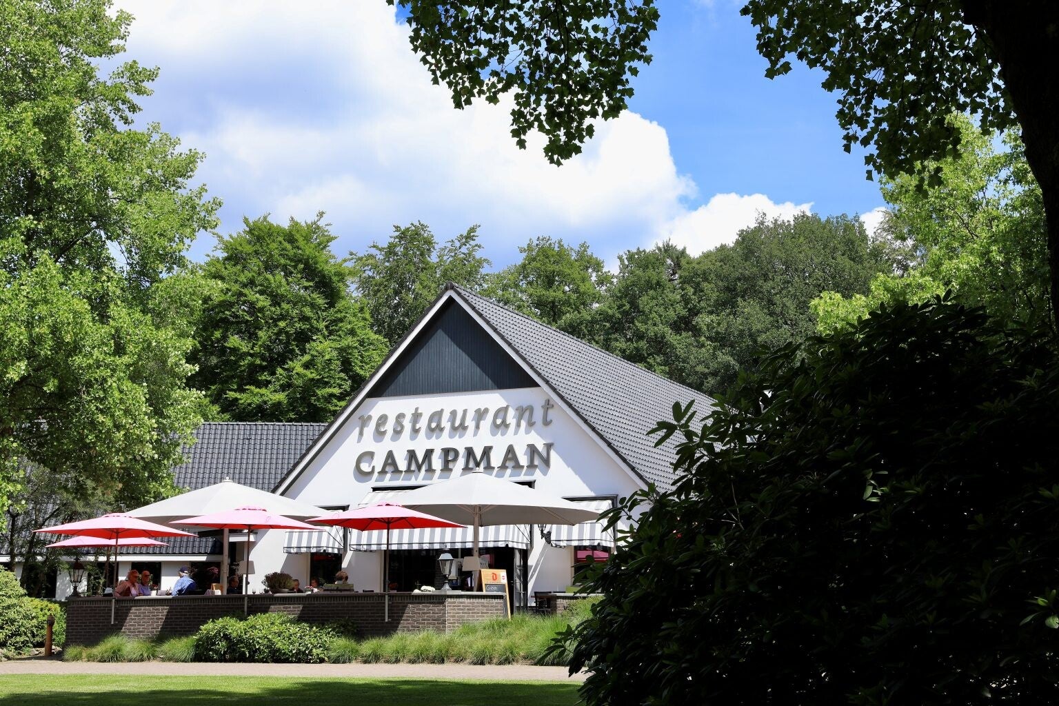 Restaurant Campman in Renkum, met een terras onder parasols en omringd door groen, waar gasten genieten van het mooie weer.