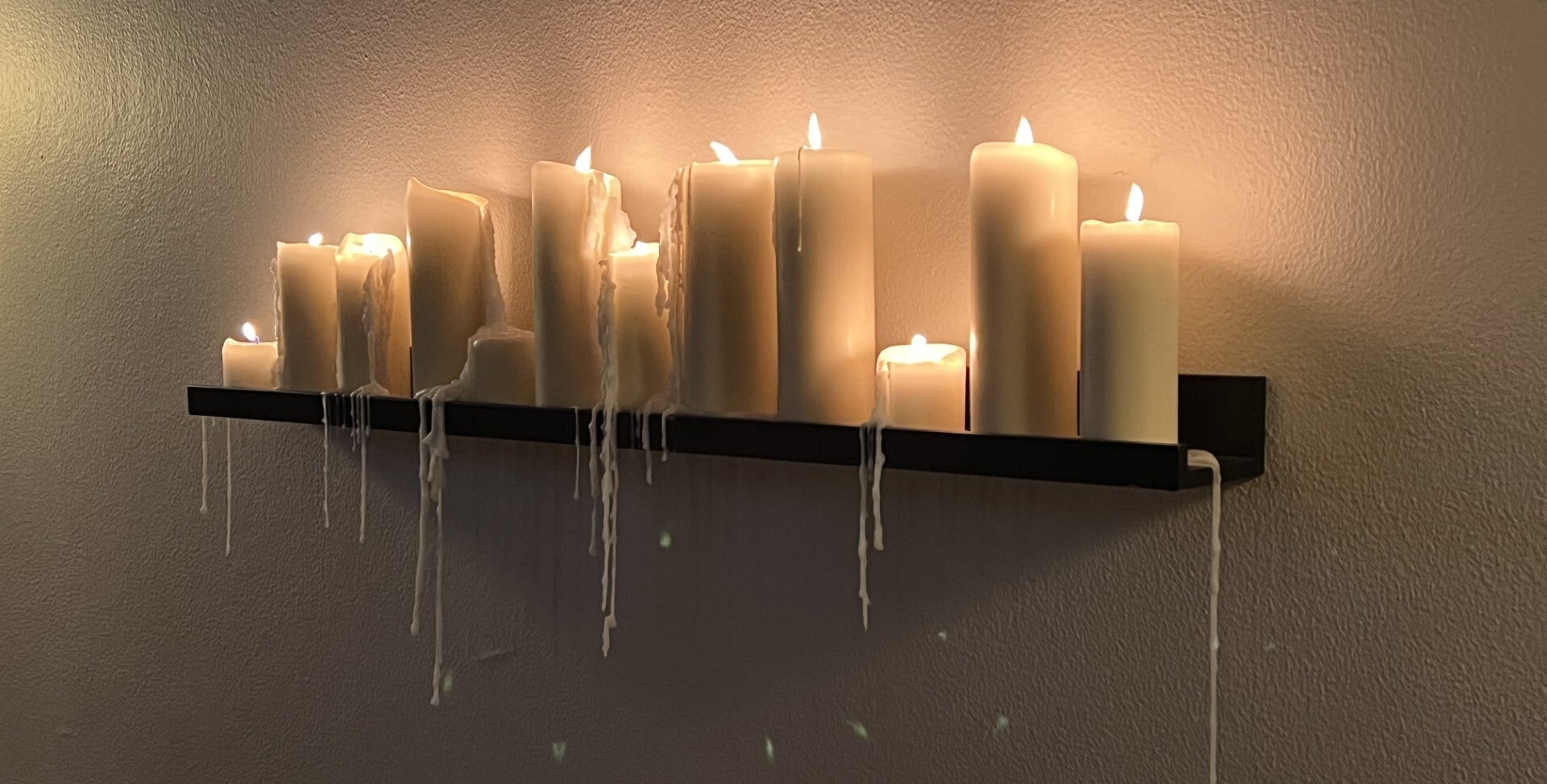 Brandende kaarsen op een plank tegen een muur met sierlijk druipend kaarsvet, die een warme en rustige sfeer creëren