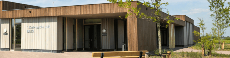 Een modern uitvaartcentrum genaamd ''t Karbrugsche Veld' van DELA, met een houten gevel en een rustige, open omgeving.