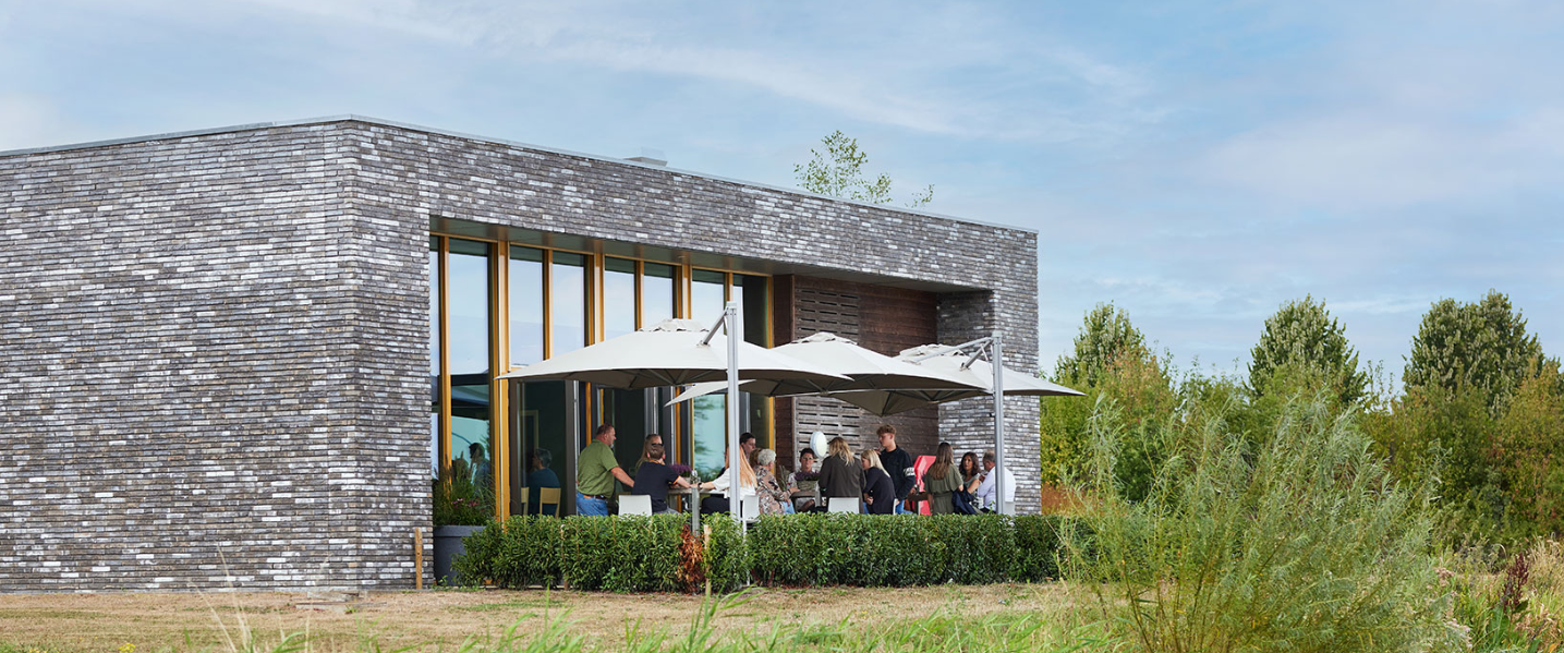 Terras met mensen en parasols in de buitentuin van een crematorium.