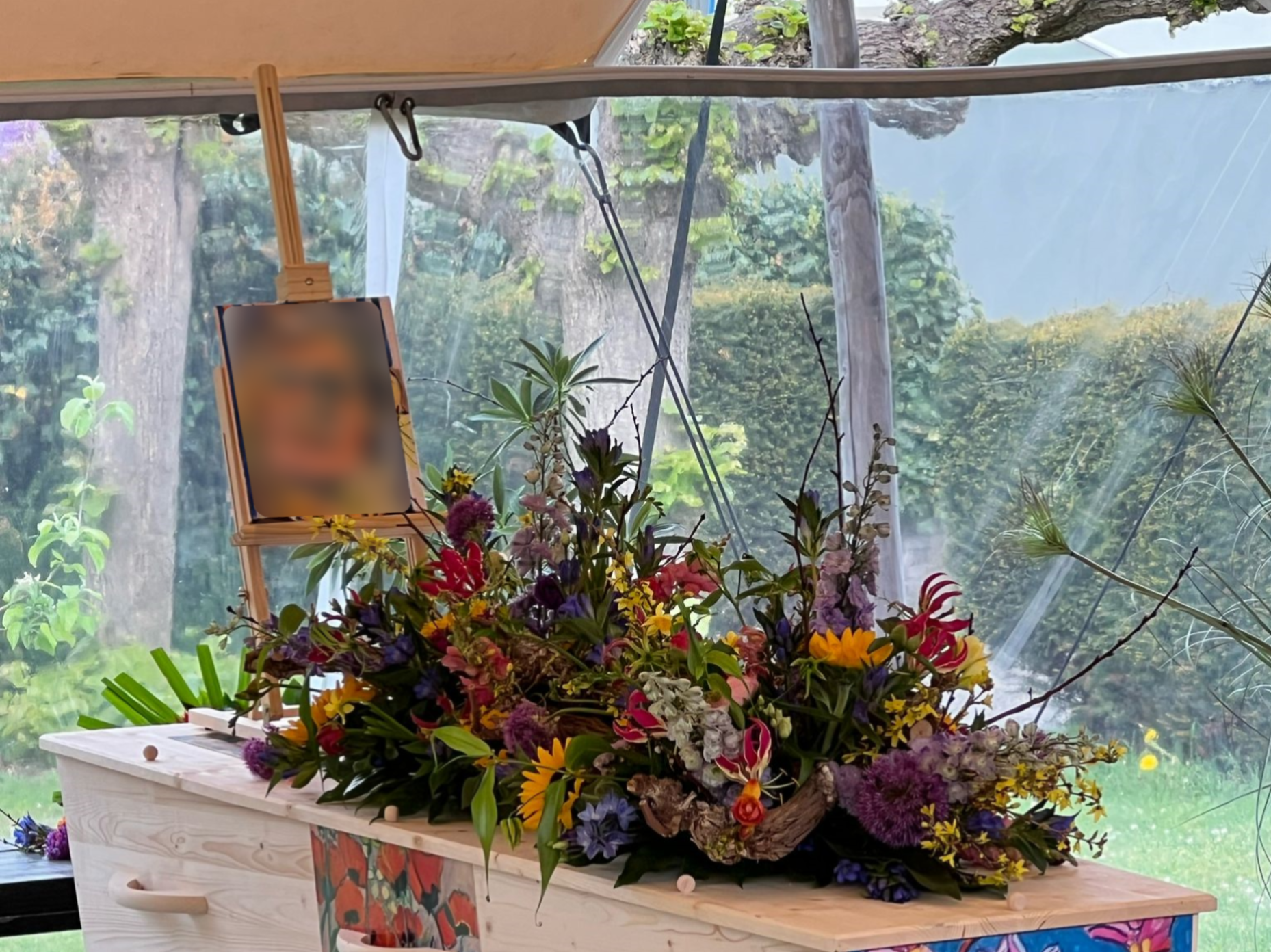 Beschilderde uitvaartkist onder een tentdok met schilderij aan het hoofd van de uitvaartkist