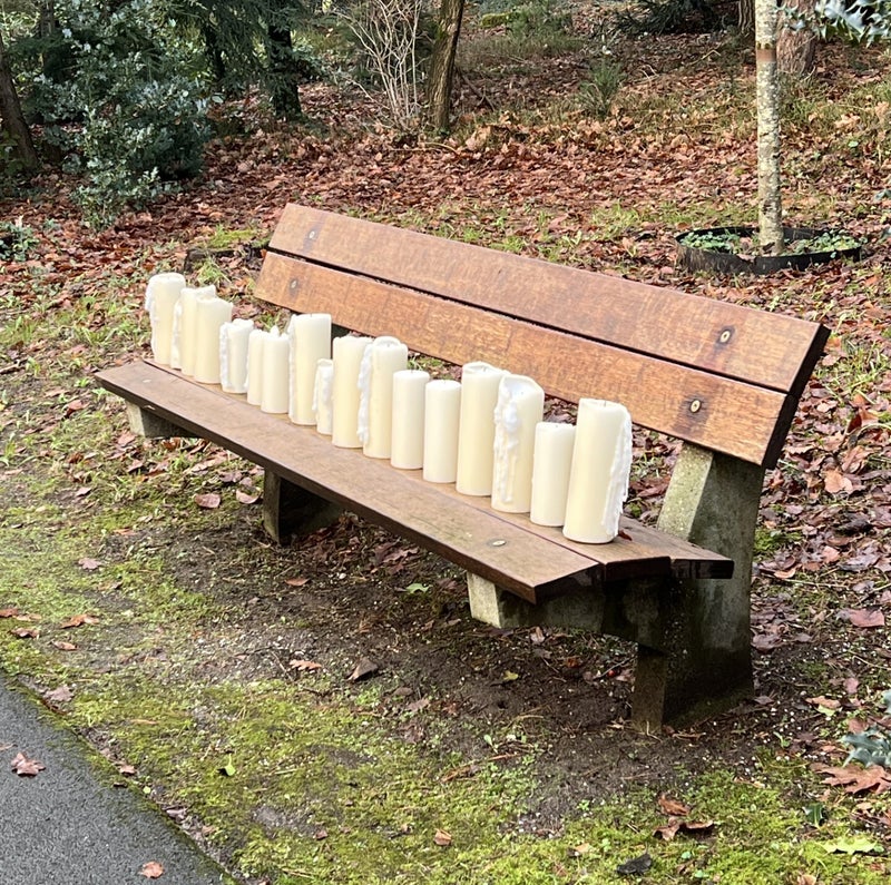 Kaarsen op een houten bankje in een herfstachtige omgeving  op een begraafplaats.