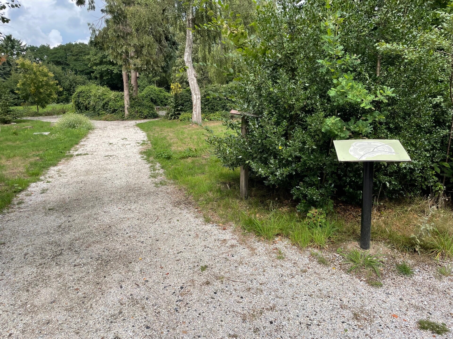 Natuurbegraafplaats Wageningen met zandpad en bomen met op de voorgrond en bord met een plattegrond van de begraafplaats.