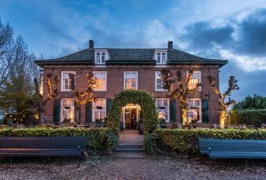 Sfeervol verlichte monumentale villa in landelijke omgeving bij schemering, met symmetrische gevel en groene toegangspoort – elegante locatie voor een stijlvolle en intieme uitvaart of herdenkingsbijeenkomst.