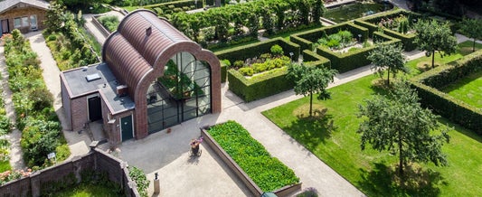 Luchtfoto van Tuinderij de Lage Oorsprong in Oosterbeek, met glazen kas, moestuin, strakke hagen en bloeiende tuinen – groene en rustgevende locatie voor een persoonlijke uitvaart of herdenkingsbijeenkomst.