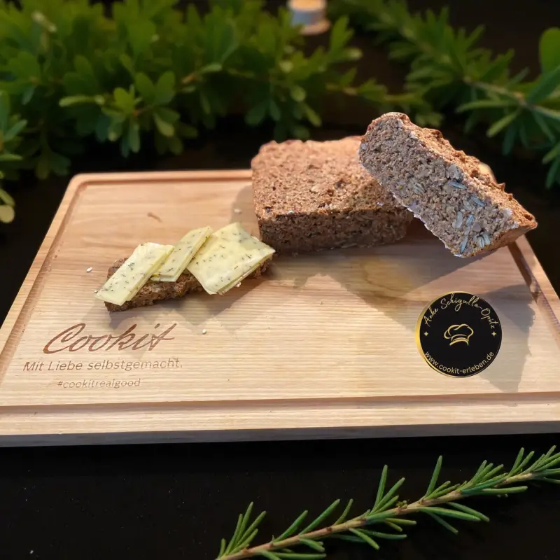 Frisch gebackenes Eiweißbrot mit Körnern, Haferkleie und Nüssen auf einem Holzbrett serviert. Gesundes Low-Carb-Brot nach dem Rezept der Ernährungs-Docs, zubereitet mit dem Cookit von Bosch.