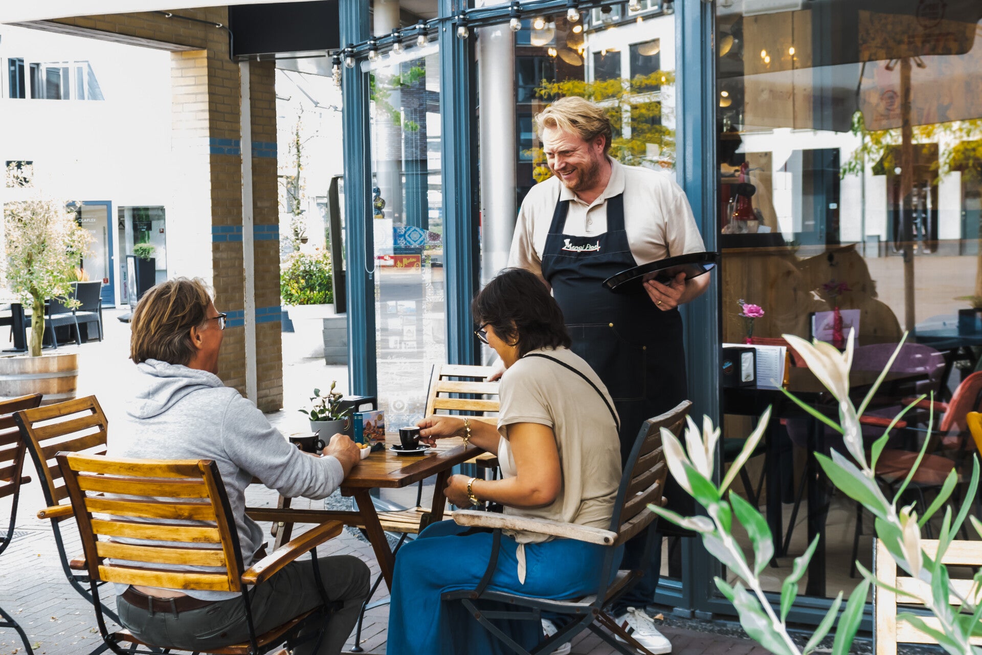 Gastvrijheid op het terras: Geertjan serveert koffie aan twee gasten bij MangiApe.