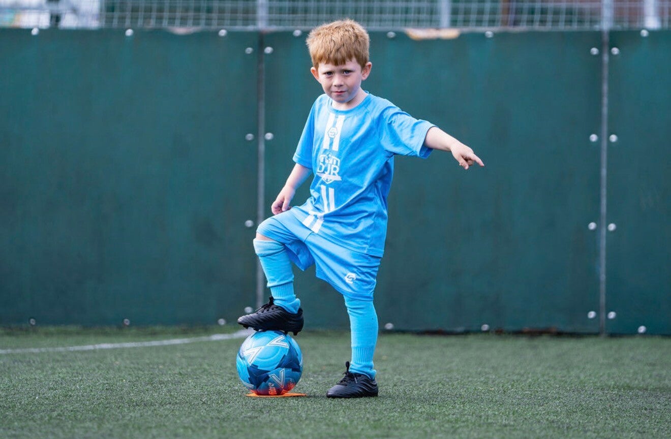 "Young children dribbling footballs through cones at a Tiny Tacklers session"