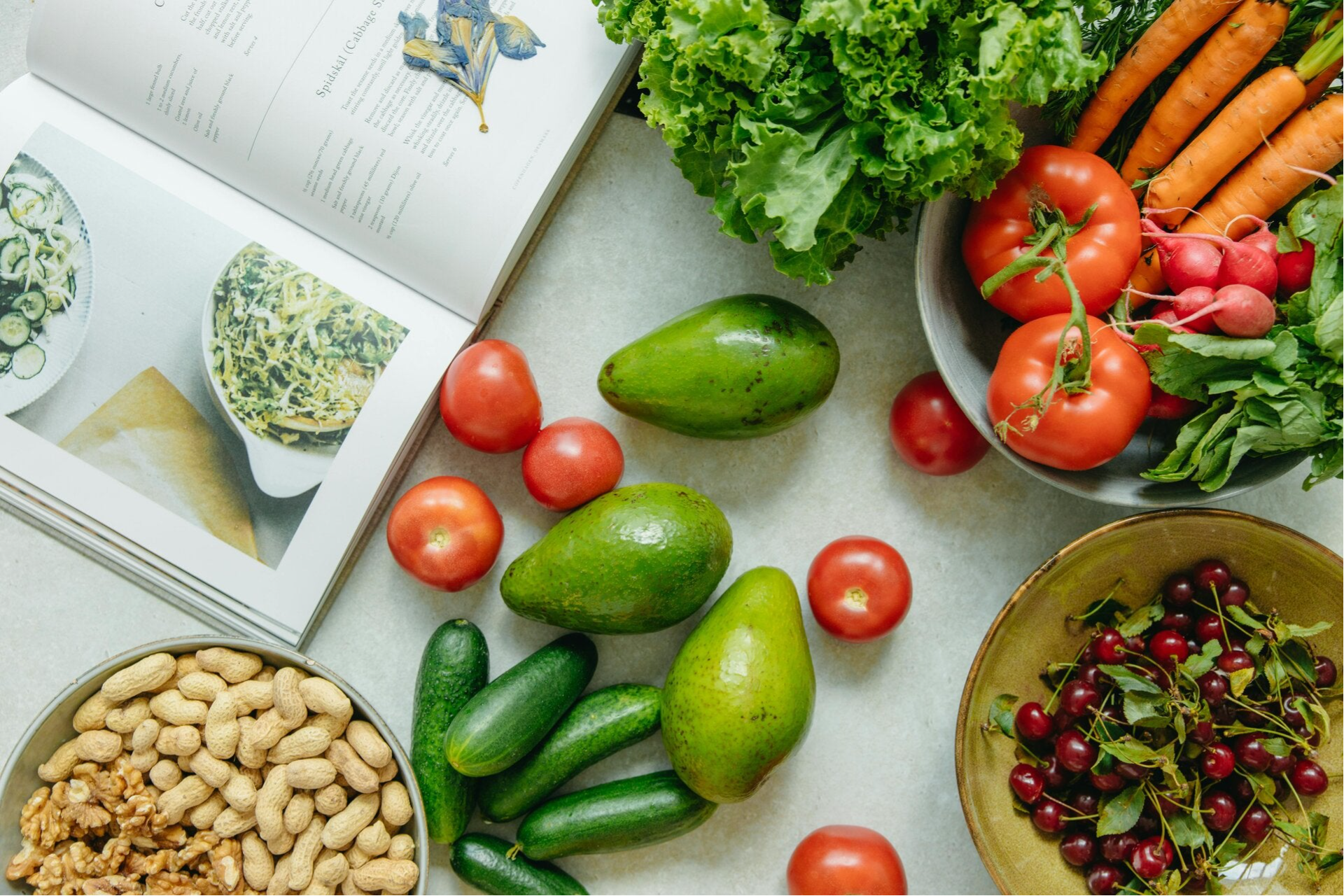 Er staan schalen met groenten, fruit, noten en vruchten samen met een kookboek met recepten op tafel