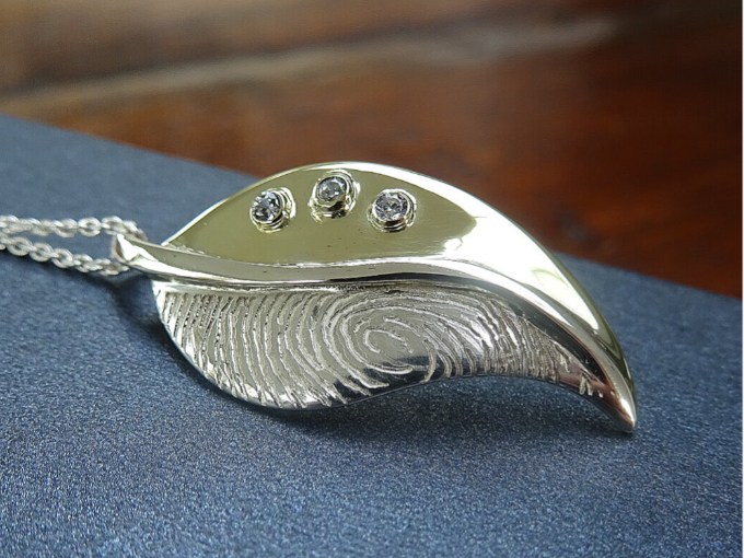 Een zilver met gouden hanger in een vorm van een blad, met een vingerafdruk en 3 witte saffieren.