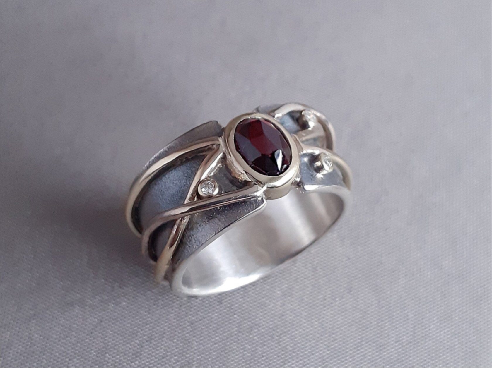 Dit is een handgemaakte ring. De basis is gemaakt van eigen zilver, met daarover draden van eigen geel en witgoud. De granaat en diamantjes zijn ook van de klant zelf. 